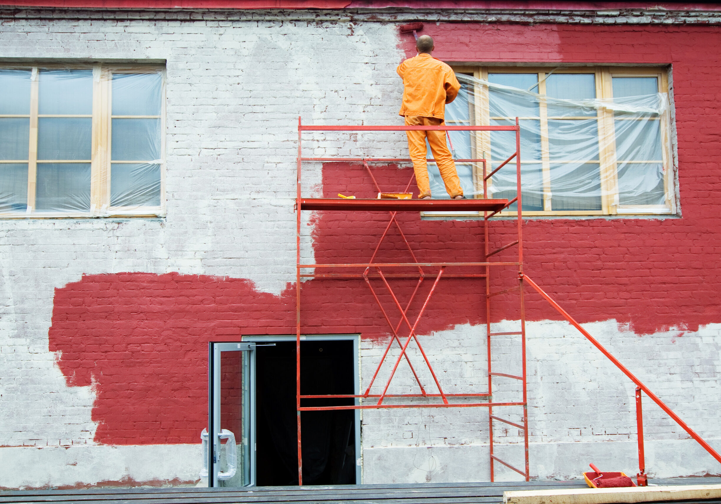 Painting in red Man painting a brick wall in red